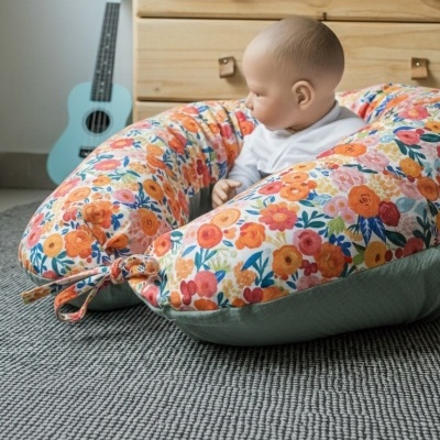 Almofada de amamentação floral com bebé sentado no chão e móvel em madeira