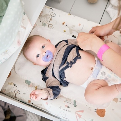 Bebé numa cama de mudança com capa estampada e adulto a ajustar roupa