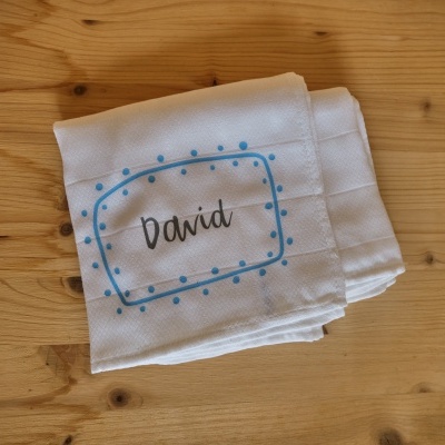 Guardanapo branco com nome David e padrão azul sobre mesa de madeira