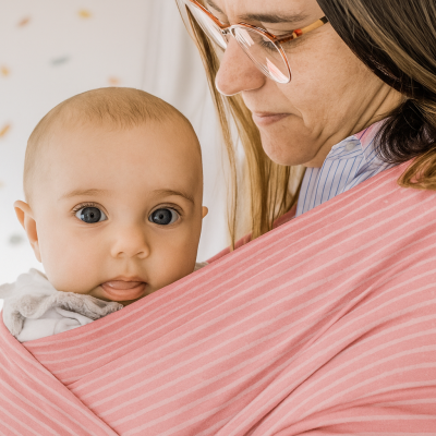 Bebé vestido de branco num sling rosa riscado transportado por adulto com óculos