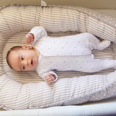 Bebé deitado num ninho de bebé acolchoado com padrão de riscas e bolinhas