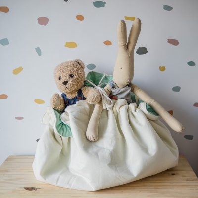 Saco de armazenamento de tecido com dois brinquedos de pelúcia numa superfície de madeira