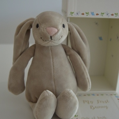 Peluche de coelho cinzento claro ao lado de caixa branca decorada e cartão 'My First Bunny'.
