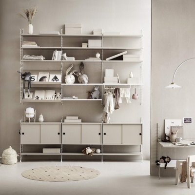 Estante modular branca com prateleiras e armários e mesa infantil com cadeiras de madeira clara em sala clara