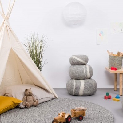 Quarto infantil com tenda bege, almofada amarela, tapete redondo cinzento e brinquedos de madeira.