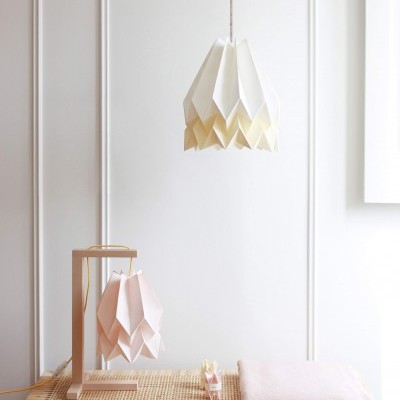 Candeeiros de origami branco e rosa sobre mesa de madeira com cobertor cor de rosa