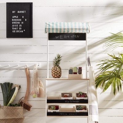 Banca infantil de madeira com toldo azul e branco e abacaxi, painel com lista de preços na parede branca