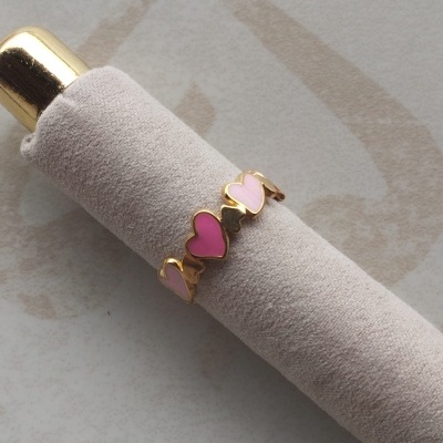 anel dourado com corações rosa numa base cilíndrica cinza claro