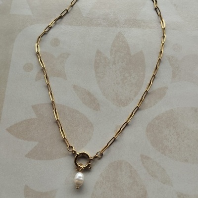 Colar dourado com pendente de pérola sobre fundo bege com padrão floral