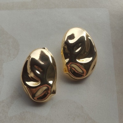 Brincos dourados metálicos com textura lisa e design assimétrico sobre fundo claro