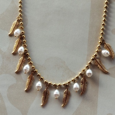 Colar dourado com penas e pérolas brancas sobre fundo bege