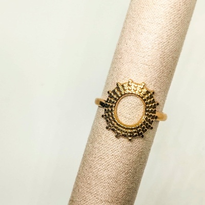 Anel dourado circular com detalhes, sobre suporte de tecido bege