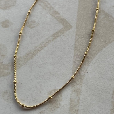 Colar dourado fino com espaçadores pequenos em fundo claro