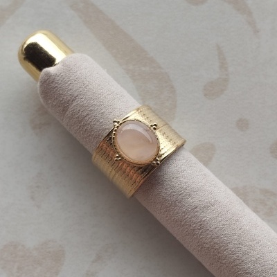 Anel dourado com pedra rosa sobre suporte felpudo bege