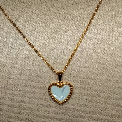 Colar dourado com pendente coração azul claro sobre tecido bege