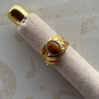 Anel dourado com pedra castanha sobre suporte bege claro