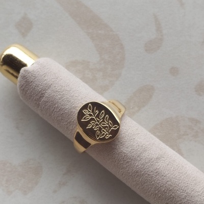 Anel dourado com desenho de folhas sobre suporte de veludo bege
