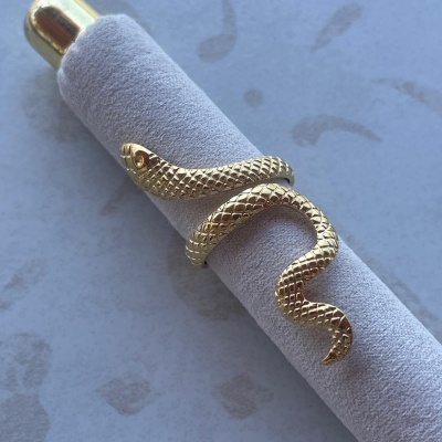 Anel dourado em forma de serpente com escamas em suporte cinzento.
