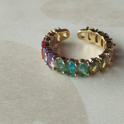Anel dourado com pedras coloridas sobre superfície clara