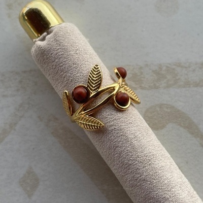 Anel dourado com folhas e pedras castanhas num suporte de tecido bege.