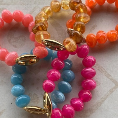 Pulseiras elásticas coloridas feitas de contas com fecho dourado sobre superfície clara