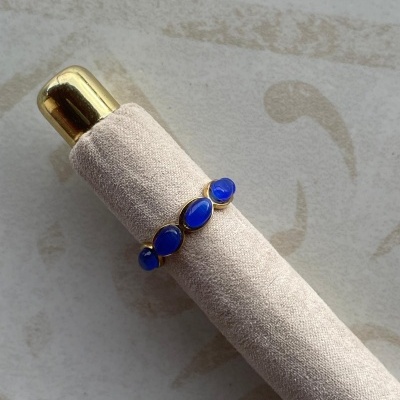 Anel dourado com pedras azuis num suporte de veludo bege.
