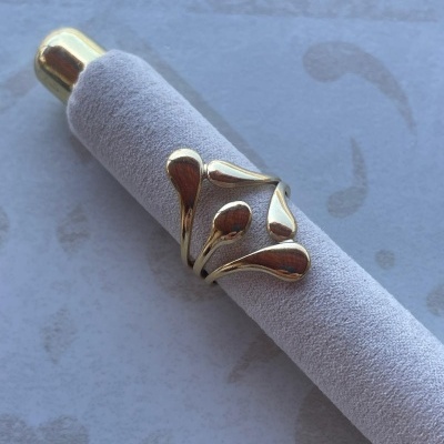 Anel dourado com design em gotas exibido num suporte de veludo cinza