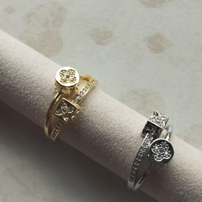 Dois anéis elegantes dourado e prateado com cristais, expostos em suporte creme