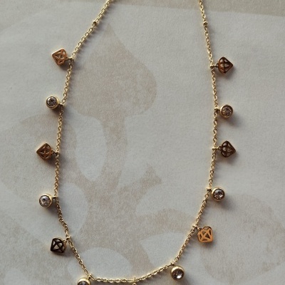 Colar dourado com pingentes de diamantes e elementos geométricos sobre fundo bege
