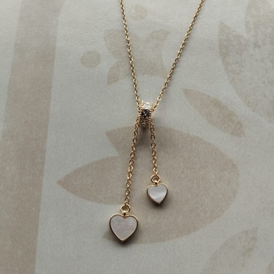 Colar dourado com pendentes de coração branco em fundo bege floral