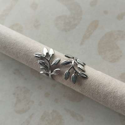 Anel prateado com design de folhas sobre suporte de veludo bege.