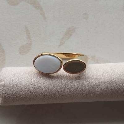 Anel dourado com detalhes ovais branco e castanho sobre suporte de veludo