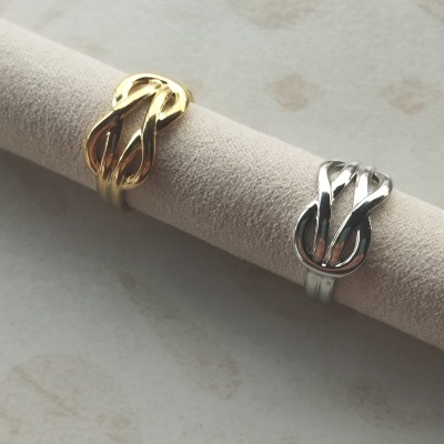 Dois anéis entrelaçados, dourado e prateado, em suporte de tecido cinzento claro