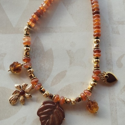 Colar com contas laranja e douradas e vários pendentes decorativos.