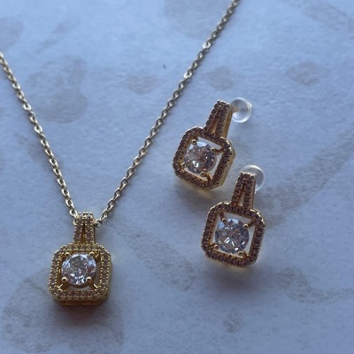 Conjunto de joalharia dourado com pedra brilhante em fundo claro