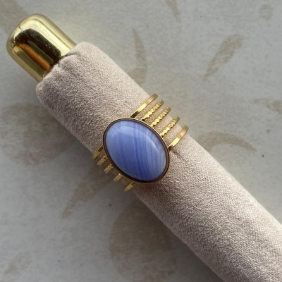Anel dourado com pedra azul clara em suporte de veludo bege e topo dourado.