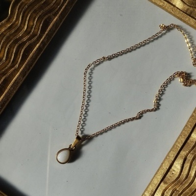 Colar dourado com pendente de pedra branca numa moldura dourada texturada