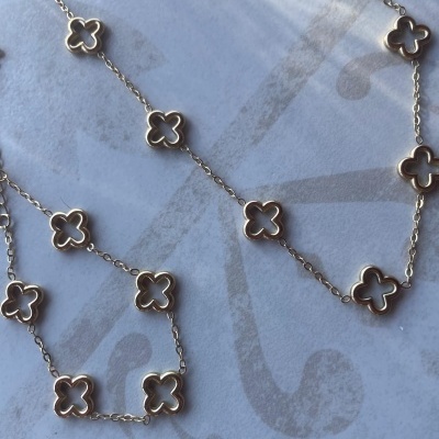 Conjunto de joalharia dourada com flores vazadas em fundo claro.