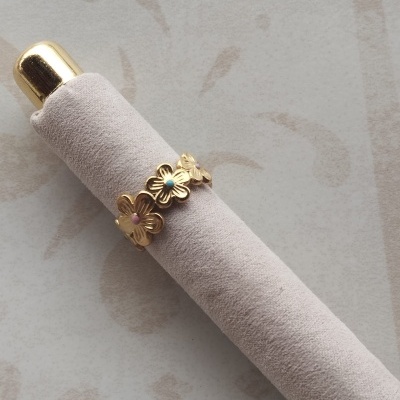 Anel dourado com três flores coloridas em suporte cinza claro
