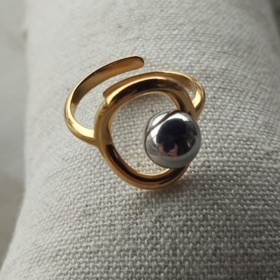 Anel metálico dourado com esfera prateada sobre tecido bege