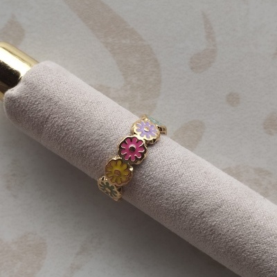 Anel dourado com flores esmaltadas amarelas e vermelhas sobre suporte de veludo cinza.