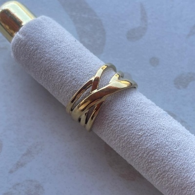 Anel dourado entrelaçado em rolo cinza aveludado sobre superfície clara