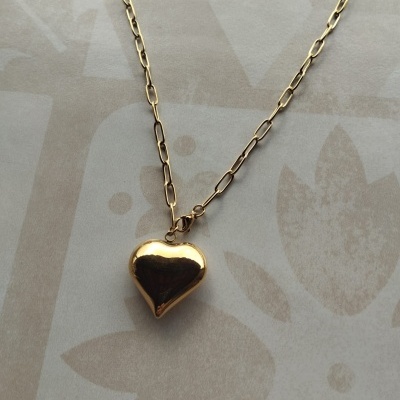 Colar dourado com pendente coração em fundo floral bege
