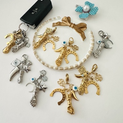 Pendentes dourados e prateados com símbolos de sorte e proteção sobre fundo branco.