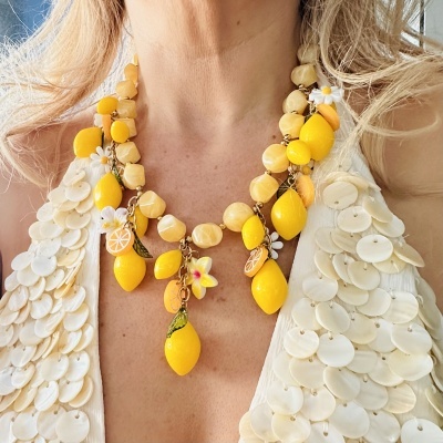 Colar amarelo com pedras e pendentes de limão, flores brancas, vestido branco com adorno de discos redondos