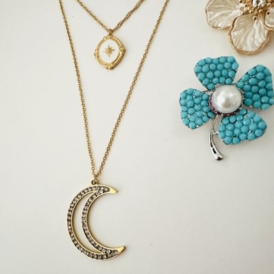 Colar dourado com pendentes e broches em forma de flor azul e branca.