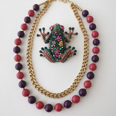 Colares coloridos e broche de rã com pedras brilhantes sobre fundo branco