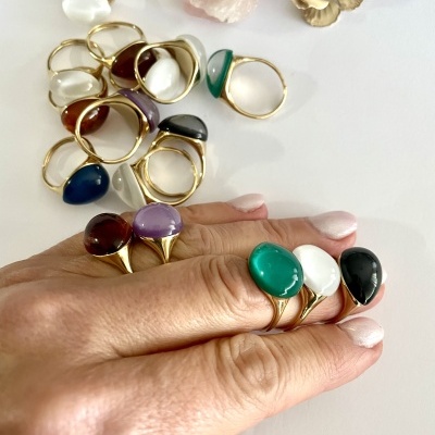 Anel de metal dourado com pedras coloridas em mão e sobre mesa com acessórios