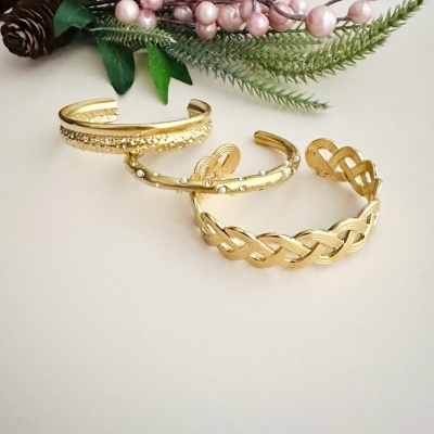 Três pulseiras douradas com padrões diferentes sobre fundo claro com decoração natural ao fundo