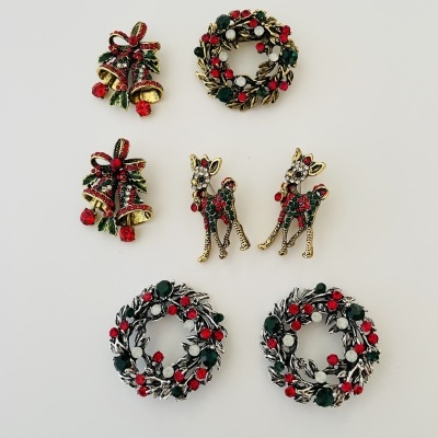 Sete broches natalinos dourados com esmalte vermelho, verde e branco sobre fundo branco.